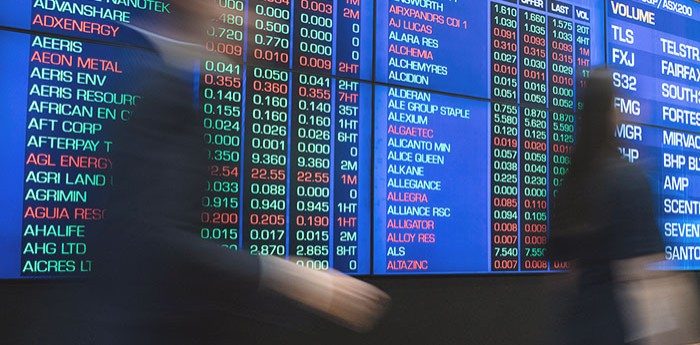 Photo of people walking past a financial data board.