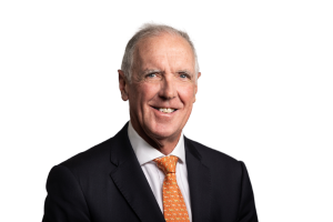 Studio head‑and‑shoulders portrait of Steve Knight wearing a dark suit jacket, white shirt, and orange tie, photographed against a plain white background.