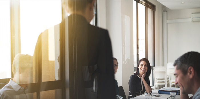 Group of people seated around a table in a meeting room viewed through glass walls