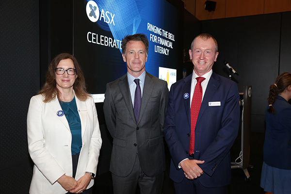 ASX CEO Helen Lofthouse, NSW Premier Chris Minns, and ASX General Manager, Investment Products and Strategy Andrew Campion, stand in front of a digital display at an ASX event. The display reads 'Ringing the Bell for Financial Literacy' and features the ASX logo. The individuals are dressed in formal business attire, and the setting is a corporate environment.