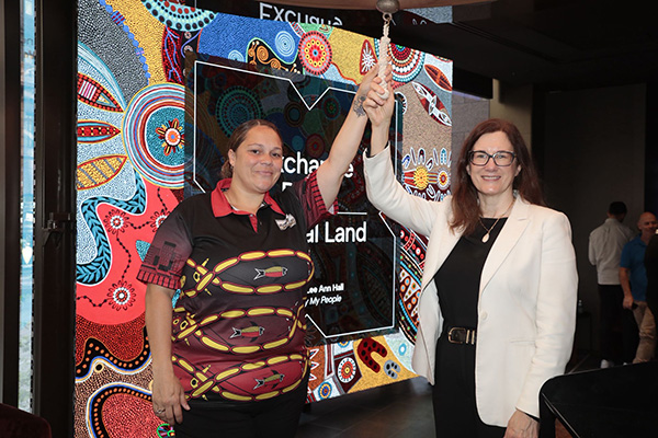 Two individuals, including ASX CEO Helen Lofthouse, stand in front of a colourful digital backdrop featuring Indigenous art. The event is an indoors ceremony to official mark the opening of ASX's new office.