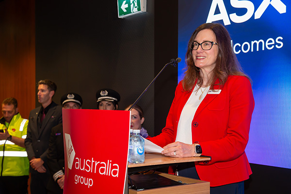 Photograph of ASX CEO Helen Lofthouse speaking at a podium during the IPO Ceremony for Virgin Australia. The event took place indoors and featured a number of colourful digital displays which are visible behind the speaker.