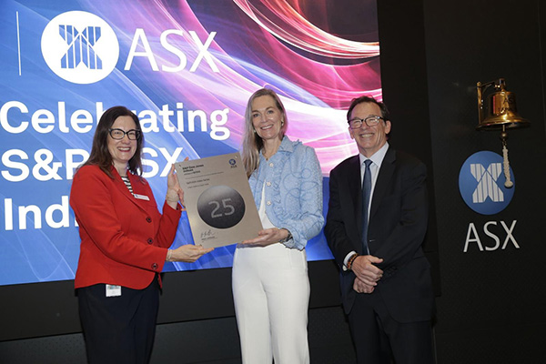 An ASX event showcasing the celebration of the S&P/ASX index milestone. The setting includes a presentation with a plaque featuring the number '25' and a bell symbolizing achievement. The backdrop displays the ASX logo and vibrant visuals in red and blue tones.
