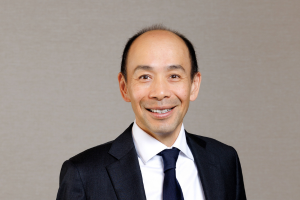 Head-and-shoulders professional portrait of Darren Yip wearing a collared shirt and blazer, facing the camera against a plain light background