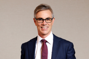  Head-and-shoulders professional portrait of Andrew Jones wearing glasses and a collared shirt with a blazer, facing the camera against a plain light background