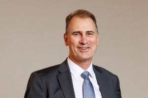 Head-and-shoulders professional portrait of Andrew Tobin wearing a suit jacket and tie, facing the camera against a plain light background