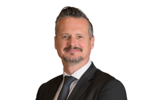 Head-and-shoulders professional portrait of Jamie Crank wearing a suit jacket, facing the camera against a plain light background