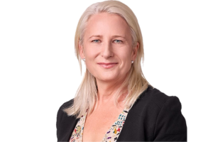 Head-and-shoulders professional portrait of Lucinda McCann wearing a patterned top and blazer, facing the camera against a plain light background