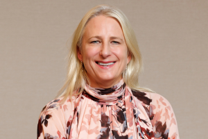 Head-and-shoulders professional portrait of Lucinda McCann wearing a patterned top and blazer, facing the camera against a plain light background