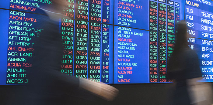 Electronic trading screens displaying stock codes, prices, and numerical market data, with blurred figures moving in the foreground.