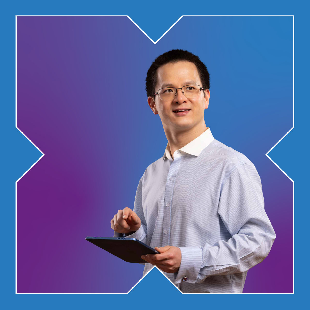 A square photo of a man holding a tablet and smiling into the distance.