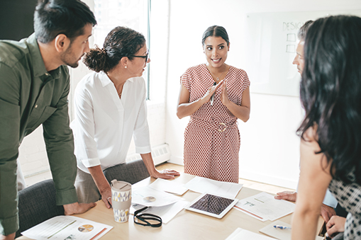 Group of people standing around a table reviewing documents and a laptop in a bright room