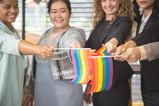 Group of people standing side by side holding small rainbow flags indoors