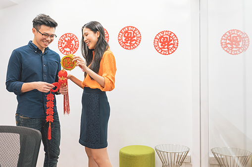 Two people standing indoors holding red decorative ornaments against a white wall