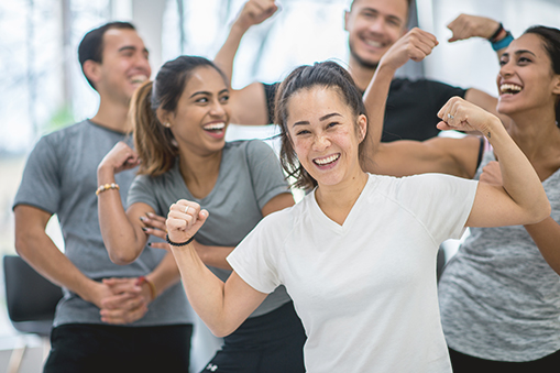 Group of people standing indoors with arms raised and bent in a coordinated pose
