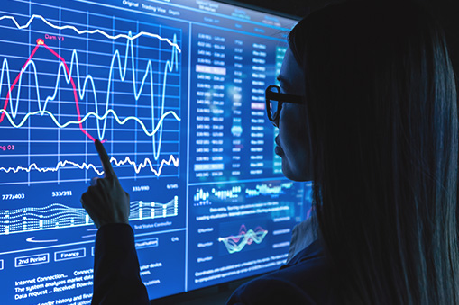 Person viewed from behind looking at digital screens displaying charts and data