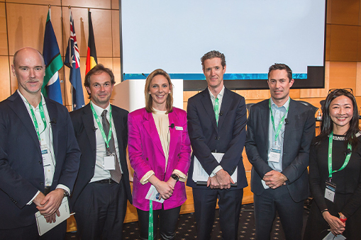 Group of people standing together indoors with flags and a presentation screen in the background