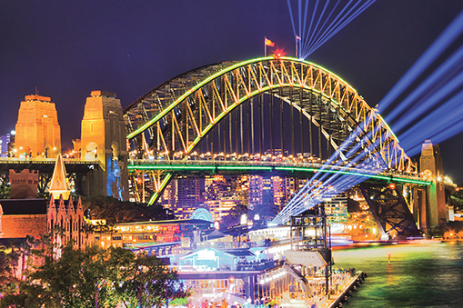 Sydney Harbour Bridge illuminated at night with city lights and water in the foreground