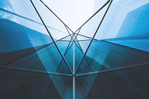 Interior view of a glass building with intersecting steel beams and reflective surfaces