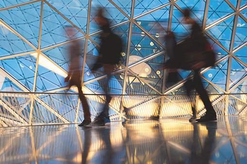 Blurred silhouettes of people walking through a glass‑roofed building