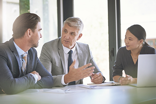 Three people seated at a table engaged in discussion with a laptop and documents