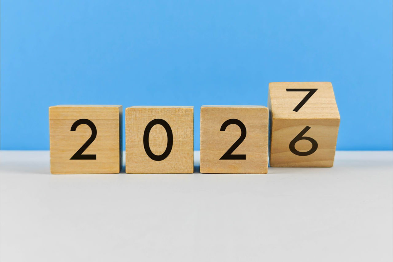 Four wooden cubes display the digits of the year 2026 turning into 2027 against a bright blue background. 
