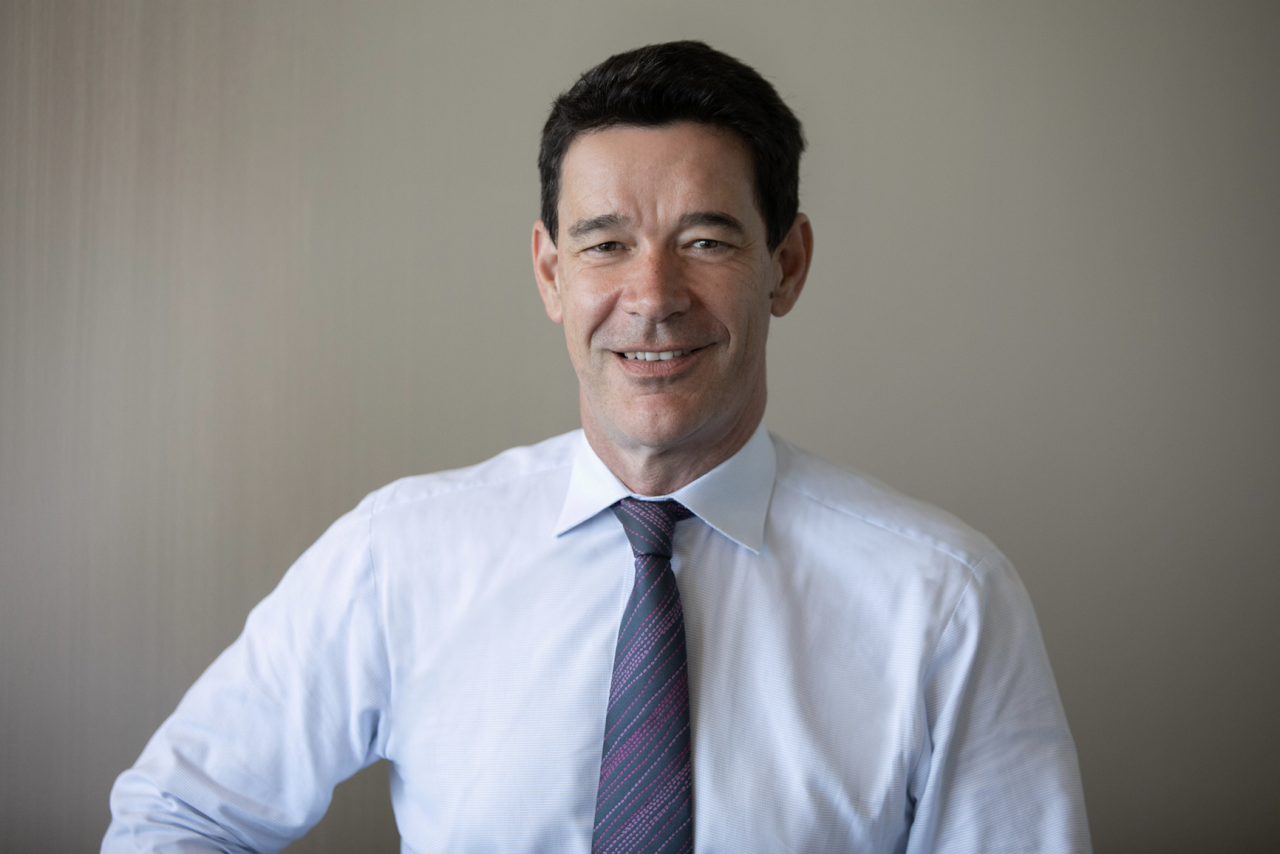 Head-and-shoulders portrait of a person wearing a light blue shirt and patterned tie against a plain background.
