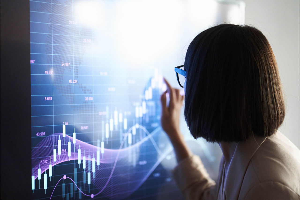 A female is closely examining a large digital screen displaying a complex financial chart. 
