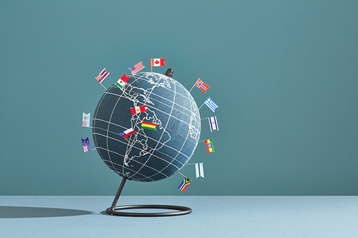 Globe on a stand surrounded by small national flags against a blue background.