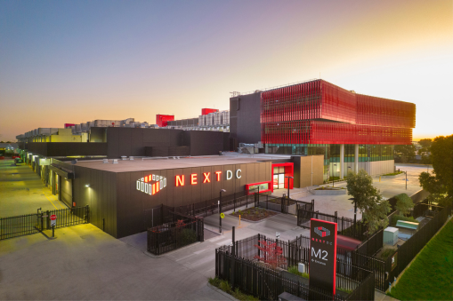 NEXTDC data centre facility with modern warehouse-style buildings and a gated entrance at sunset.