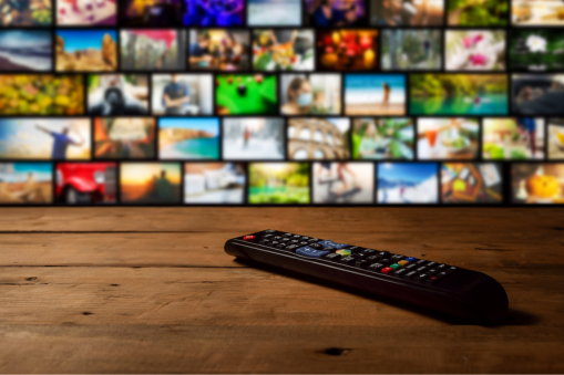 Television remote control on a wooden table with multiple television screens displayed in the background.