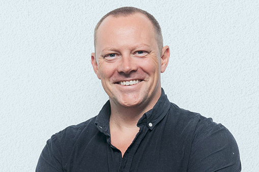 Professional headshot of an individual in a dark shirt against a neutral background