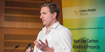 Speaker presenting at the Australasian Emissions Reduction Summit, with signage referencing carbon market initiatives and next-generation carbon credits and projects.