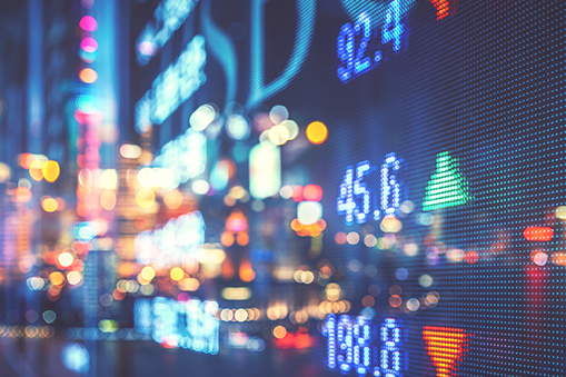 Digital display showing market data with numerical values, directional indicators and illuminated graphics against a blurred city background.