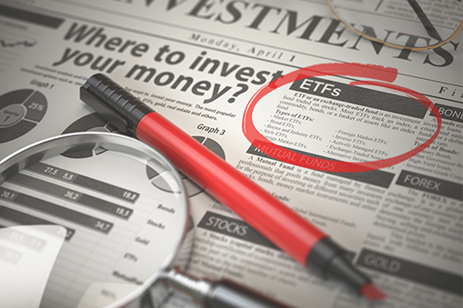 Financial newspaper page with the headline Where to invest your money, featuring a section on ETFs circled in red, alongside a red pen, printed charts and a magnifying glass placed on the page