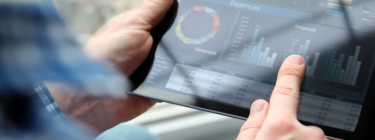 Hands holding a tablet displaying a dashboard with charts, graphs, and tabular data.