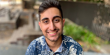 Head-and-shoulders professional portrait of a person wearing a patterned shirt, photographed outdoors with a softly blurred background