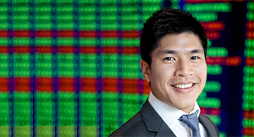 Head-and-shoulders professional portrait of a person wearing a suit jacket and tie, positioned in front of a digital display featuring coloured vertical patterns