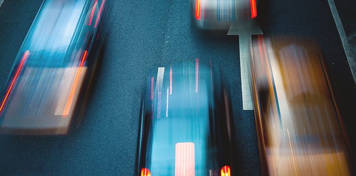 Motion-blurred view of multiple vehicles travelling along a road at night, with light streaks in red, white and blue across a dark surface