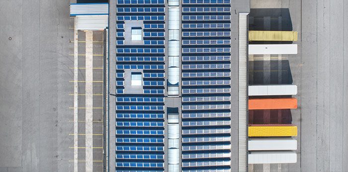 Top-down view of an industrial or logistics site with rows of solar panels and parked vehicles arranged in parallel lines on a paved surface