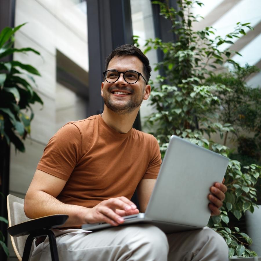 Seated person wearing a short‑sleeved top and glasses, using a laptop in a modern indoor space with plants and natural light, presented as a general visual representation of investing.