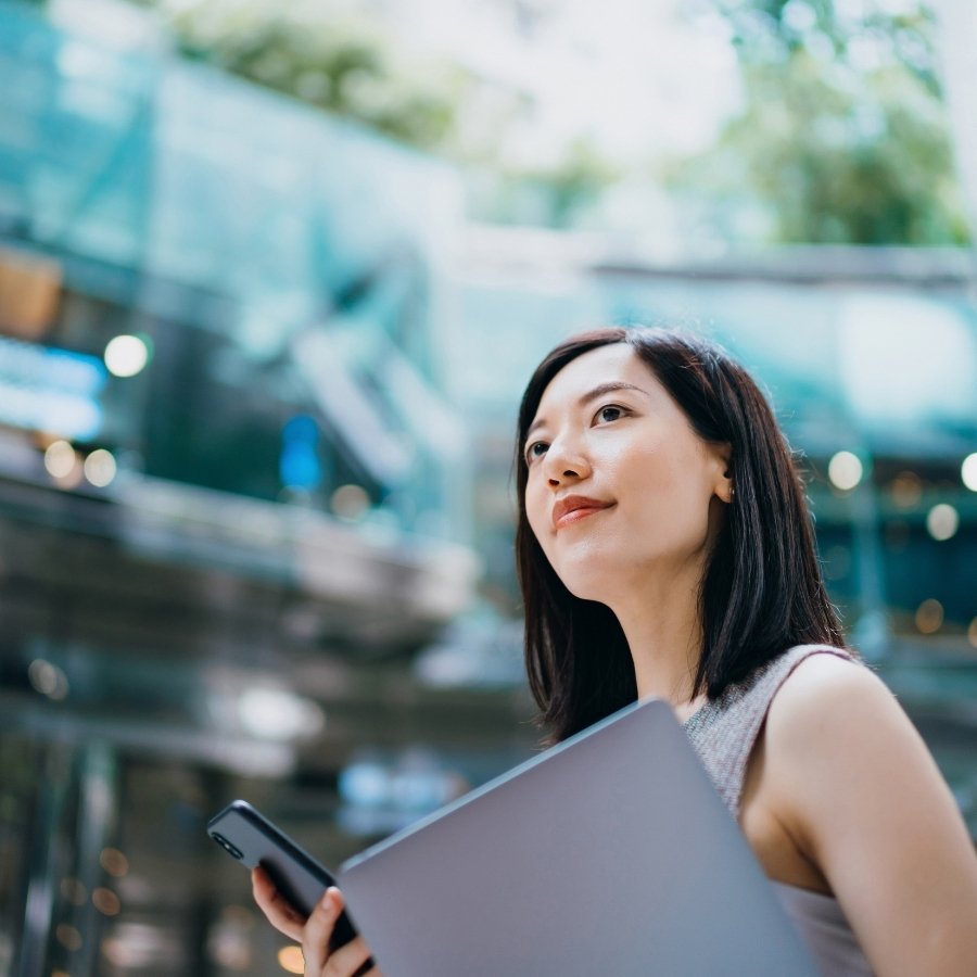 Person holding a laptop and mobile phone inside a modern glass‑walled building, with soft natural light and blurred architectural elements, used as a general visual representation of options and international ETFs.