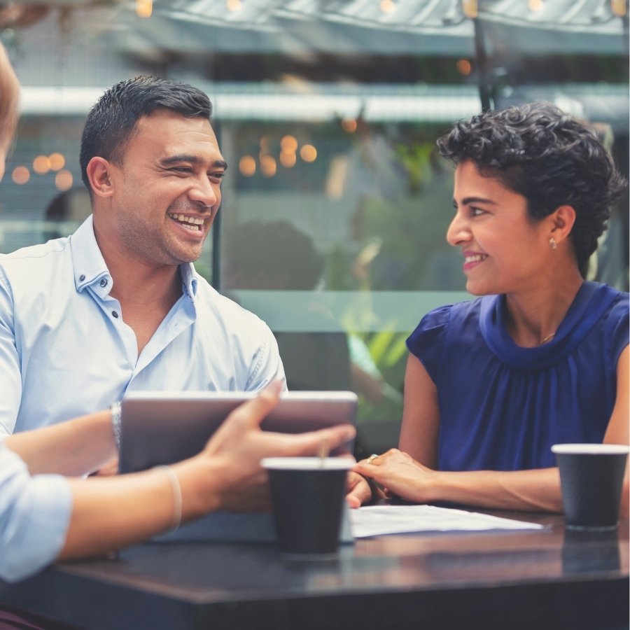 Small group seated at an outdoor table with notebooks, takeaway cups, and a tablet visible, presented as a general visual representation of investing research and discussion.
