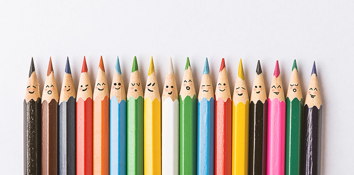 Row of coloured pencils with drawn faces on a white background