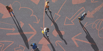 Overhead view of several people walking across a surface marked with large directional arrows.