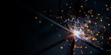 Close-up of welding in progress, with bright sparks and molten metal at the point where two metal rods meet.