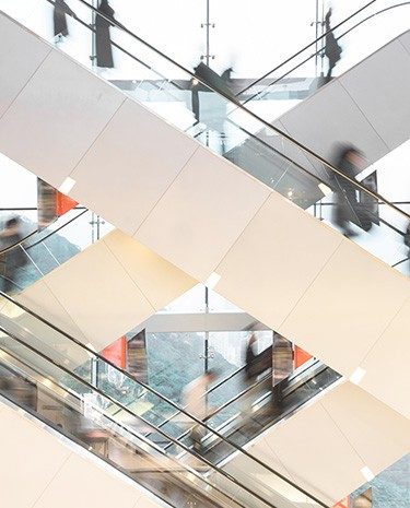 Multiple escalators crossing inside a modern building, with blurred figures moving between floors.
