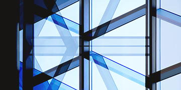 Angular architectural composition showing intersecting glass panels and metal frames with reflections in shades of blue and grey