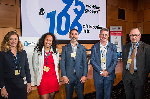 Five people standing at a conference or industry event in front of a display reading “25 working groups & 103 distribution lists”.