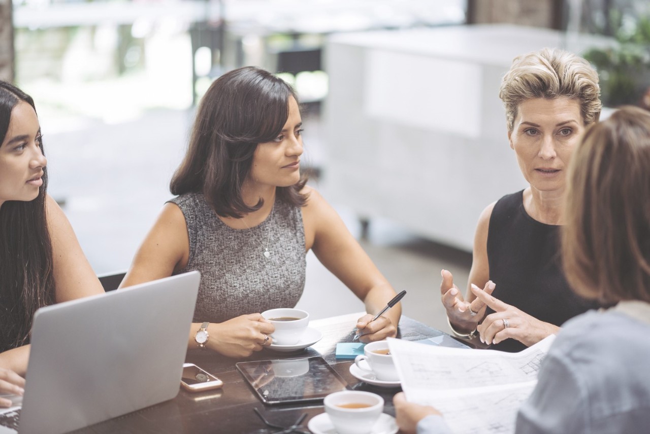 Four people seated around a table discussing documents and notes during a workplace meeting.